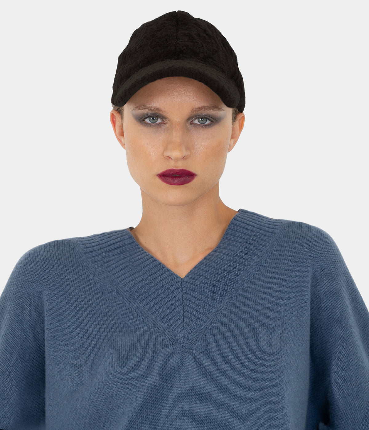 Model wearing the Dom Goor black shearling baseball cap with a blue V-neck jumper, front view