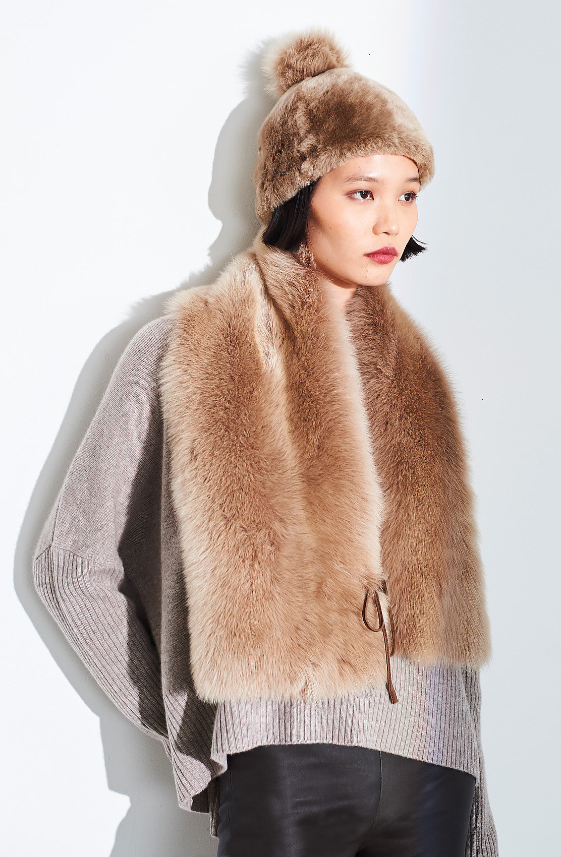 Model wearing the Dom Goor beige Toscana side tie scarf draped long, with a matching pompom hat